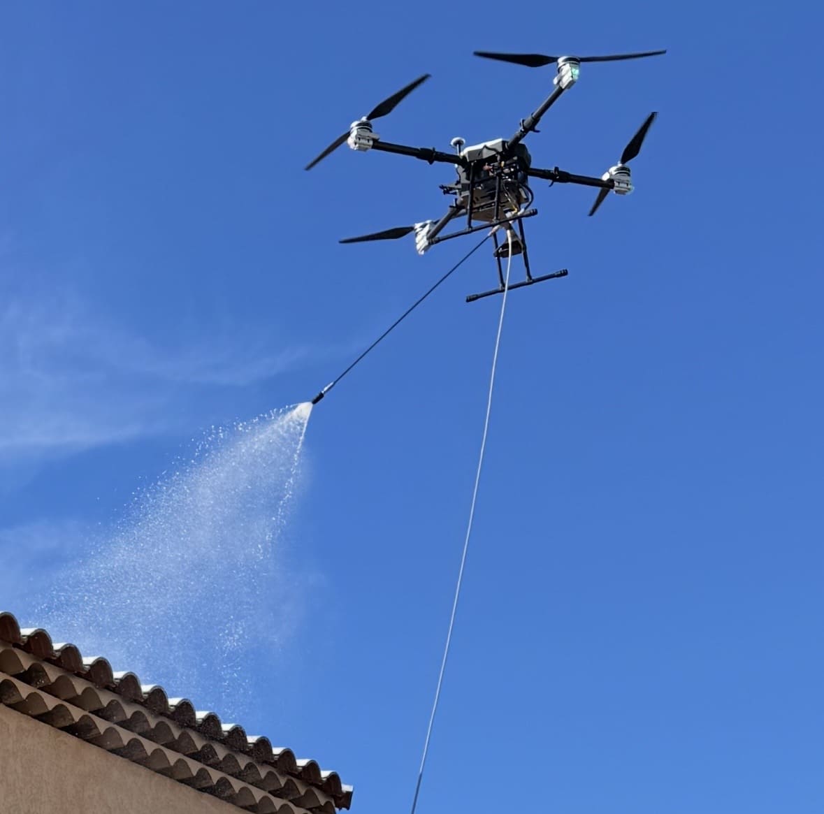 Drone Aerodronecleaner en action pulvérisant une toiture sous un ciel bleu