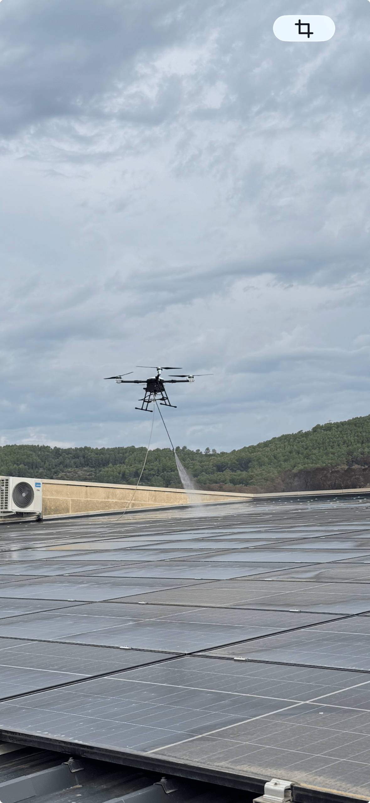 Drone Aerodronecleaner pulvérisant de l'eau pure pour nettoyer une grande centrale photovoltaïque sur toiture industrielle